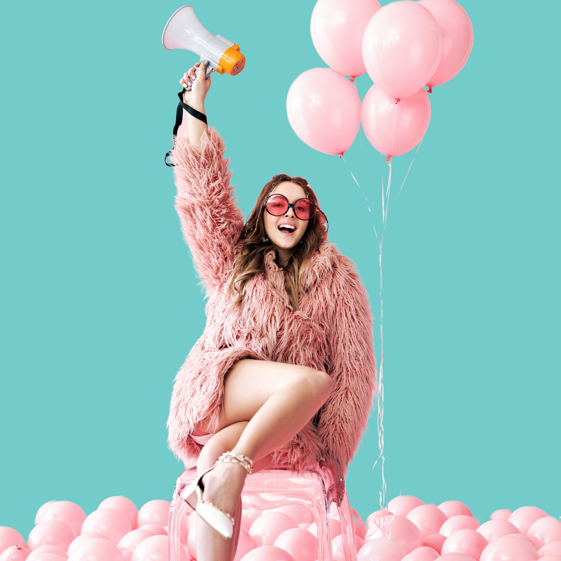A woman in a pink shaggy faux-fur coat and heart-shaped sunglasses sits on a transparent pink chair, holding a white and orange megaphone aloft. She is surrounded by numerous light pink balloons against a solid teal background.
