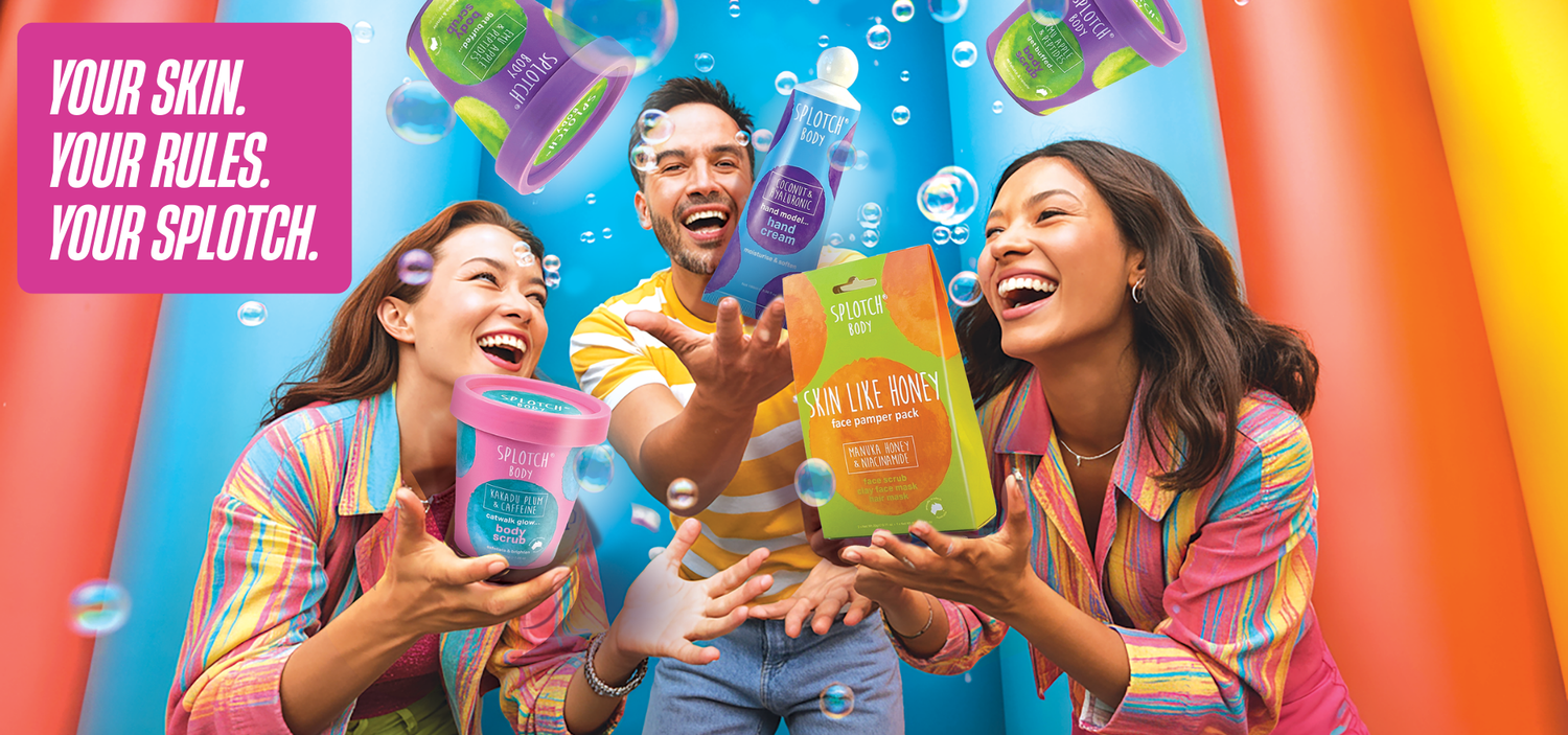 A group of three friends laughs joyfully amidst floating bubbles and colorful, oversized Splotch Body products, including a "Kakadu Plum & Caffeine" body scrub and a "Skin Like Honey" face pamper pack. A pink banner in the corner reads, "YOUR SKIN. YOUR RULES. YOUR SPLOTCH.".